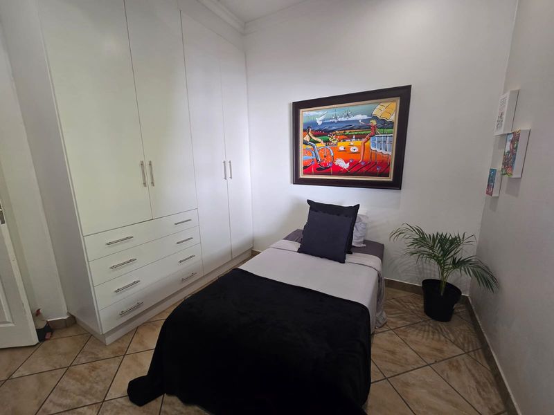A compact bedroom featuring white built-in wardrobes with ample storage and durable tiled flooring.