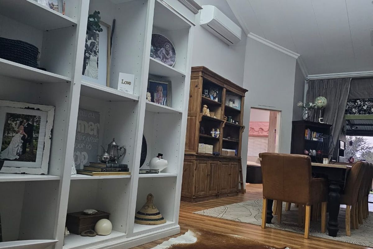 Spacious living area featuring high vaulted ceilings, built-in white shelving, and modern split-system air conditioning with warm wood-look flooring.