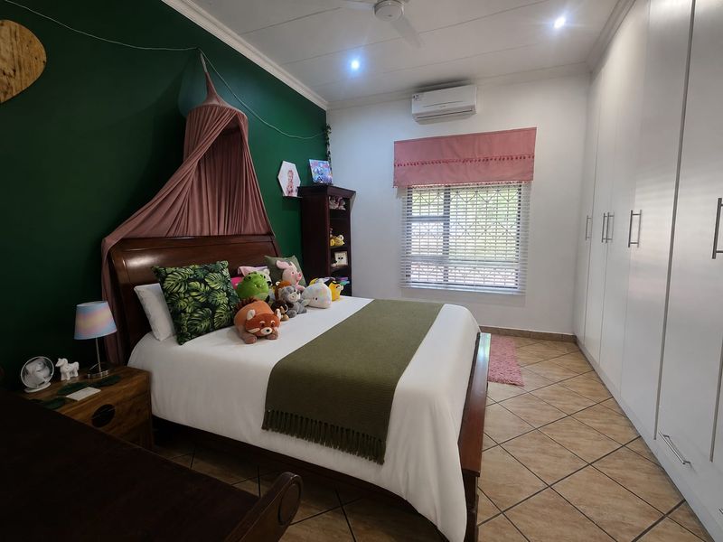 A well-maintained bedroom featuring built-in cupboards, tiled flooring, a ceiling fan, and a split-system air conditioner for climate control.