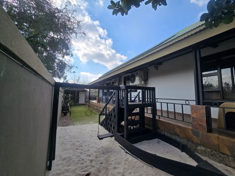 Rear exterior view featuring a covered patio with metal railings, stone cladding accents, and a landscaped garden area with a play structure.