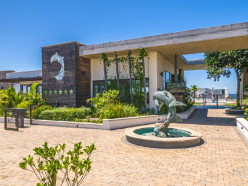 The front entrance of the apartment complex features a modern concrete canopy, a decorative dolphin water feature, and well-maintained paved landscaping.
