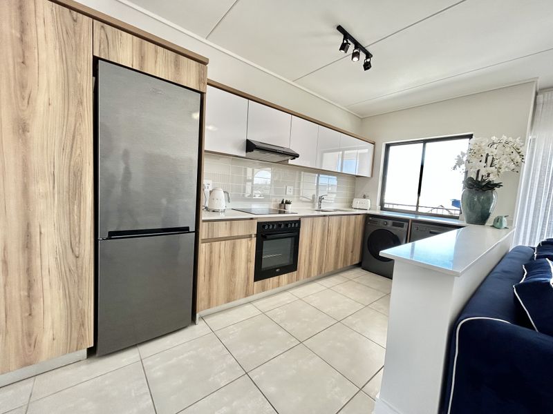 Modern kitchen featuring wood-grain and white cabinetry, integrated appliances, tiled backsplash, and sleek track lighting, offering a clean and functional culinary space.