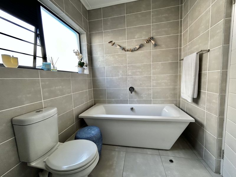 Modern bathroom featuring a freestanding bathtub, wall-mounted mixer, neutral floor-to-ceiling tiling, and a functional toilet.