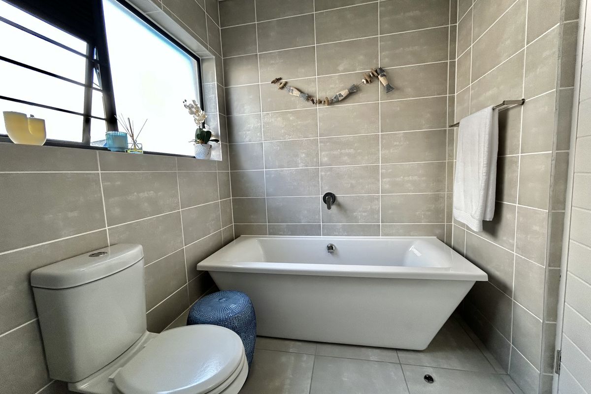 Modern bathroom featuring a freestanding bathtub, wall-mounted mixer, neutral floor-to-ceiling tiling, and a functional toilet.