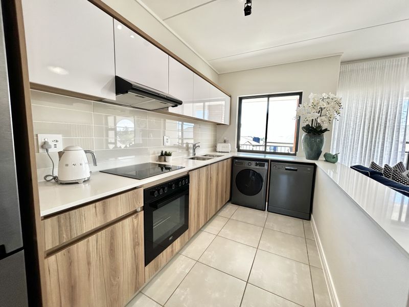 Modern galley-style kitchen featuring sleek wood-grain and white cabinetry, stone countertops, integrated appliances, and a clean subway tile backsplash.
