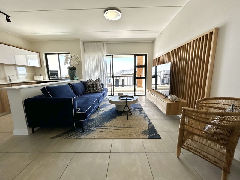 Modern open-plan living area featuring tiled floors, a timber slat feature wall, floating media console, and a sleek kitchen with stone countertops.