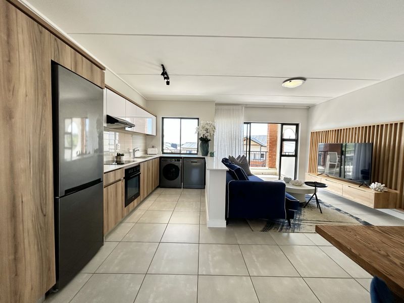 Modern open-plan kitchen and living area featuring contemporary cabinetry, integrated appliances, tiled flooring, and a stylish timber slat feature wall with balcony access.