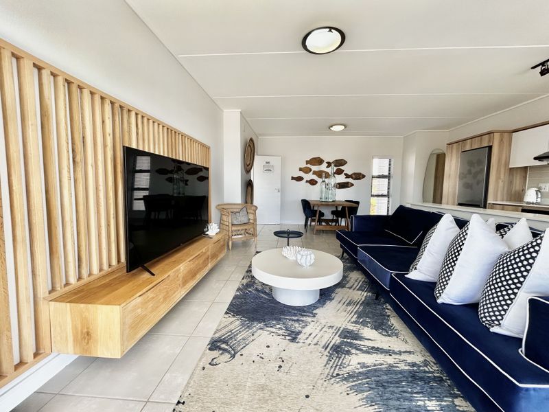 Modern open-plan living area featuring a custom timber slat feature wall, floating media console, tiled floors, and seamless flow into the kitchen space.