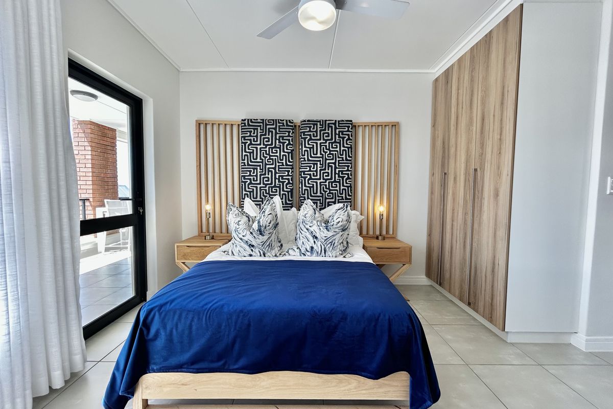 A well-maintained bedroom featuring built-in wooden cupboards, a ceiling fan, tiled flooring, and direct access to a balcony through a sliding glass door.