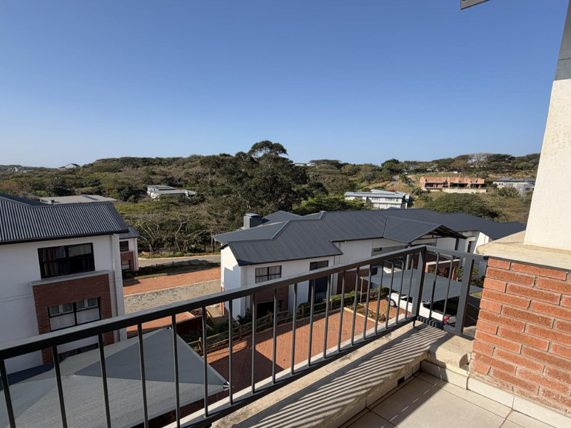 A spacious balcony featuring a metal balustrade and tiled flooring, offering elevated views of the surrounding residential estate and natural landscape.