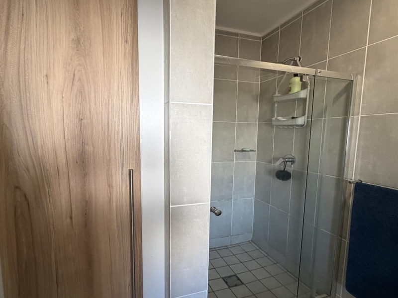 A functional bathroom featuring a glass-enclosed shower with neutral wall tiling and integrated wooden cabinetry.