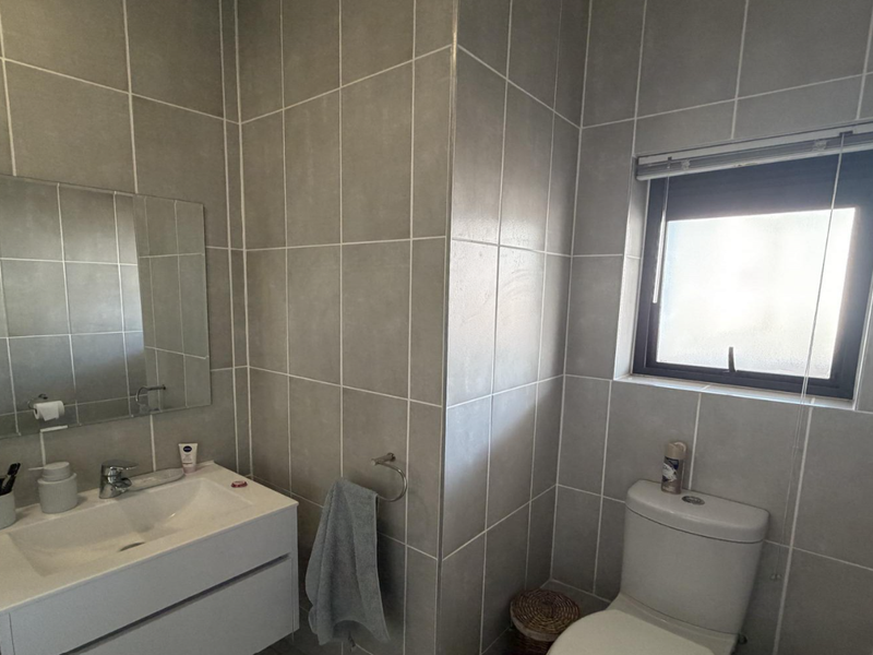 Modern bathroom featuring grey wall tiles, a wall-mounted vanity with integrated basin, and a toilet, illuminated by a frosted glass window.