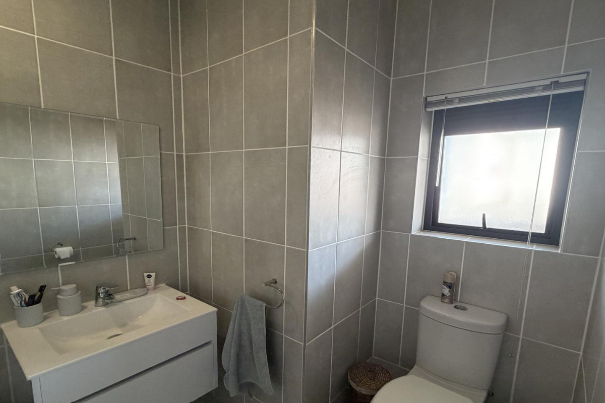 Modern bathroom featuring grey wall tiles, a wall-mounted vanity with integrated basin, and a toilet, illuminated by a frosted glass window.