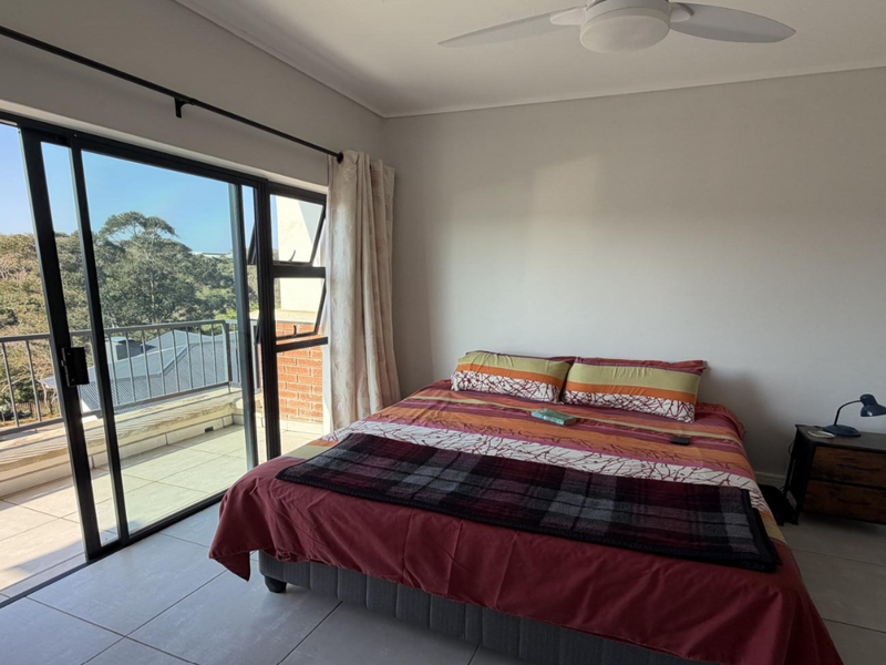 A bright bedroom featuring tiled flooring, a ceiling fan, and large sliding glass doors that open onto a private balcony with scenic views.