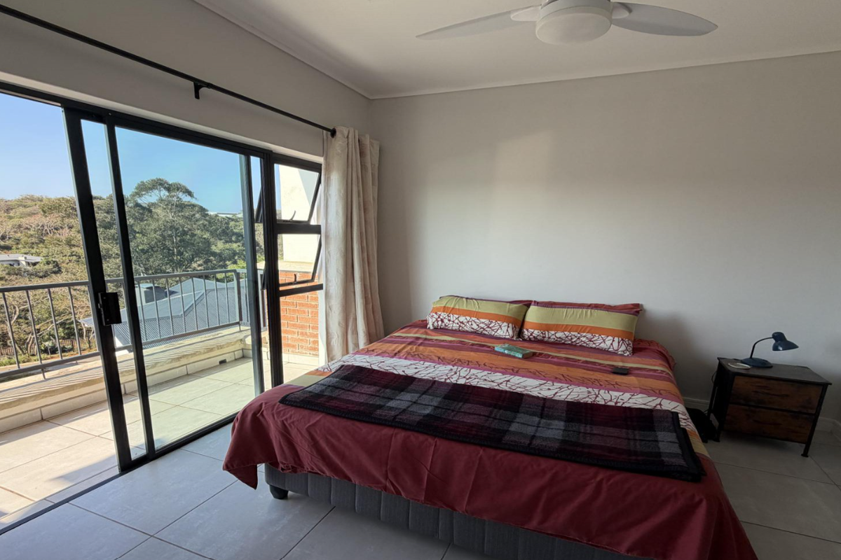 A bright bedroom featuring tiled flooring, a ceiling fan, and large sliding glass doors that open onto a private balcony with scenic views.