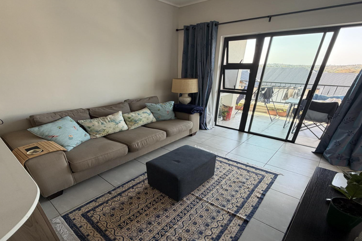 A bright living room featuring tiled flooring and a large sliding glass door that provides access to an outdoor balcony area.