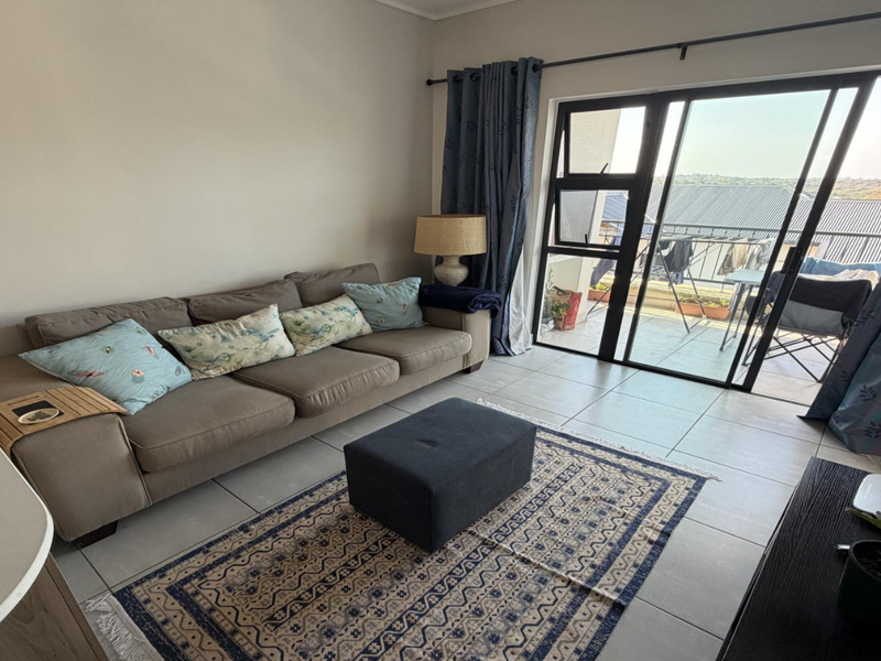 A bright living room featuring tiled flooring and a large sliding glass door that provides access to an outdoor balcony area.