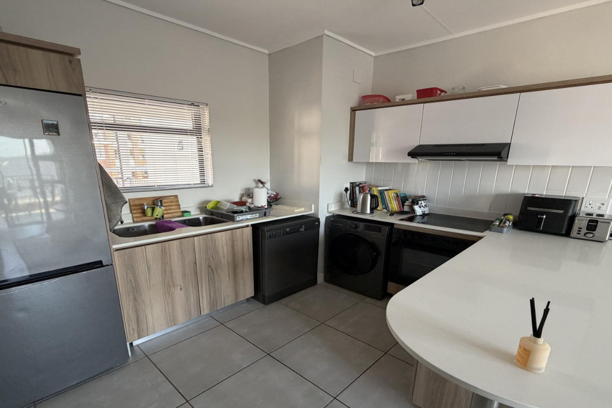 Modern kitchen featuring sleek white and wood-grain cabinetry, stone countertops, integrated appliances, and tiled flooring, offering a clean and functional workspace.