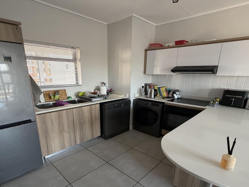 Modern kitchen featuring sleek white and wood-grain cabinetry, stone countertops, integrated appliances, and tiled flooring, offering a clean and functional workspace.