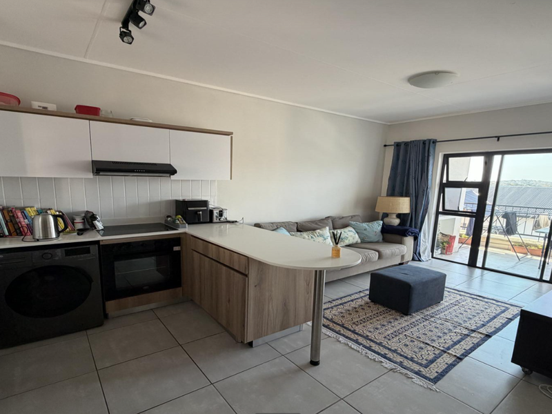 Modern open-plan kitchen and living area featuring sleek cabinetry, integrated appliances, tiled flooring, and direct access to a balcony through sliding glass doors.