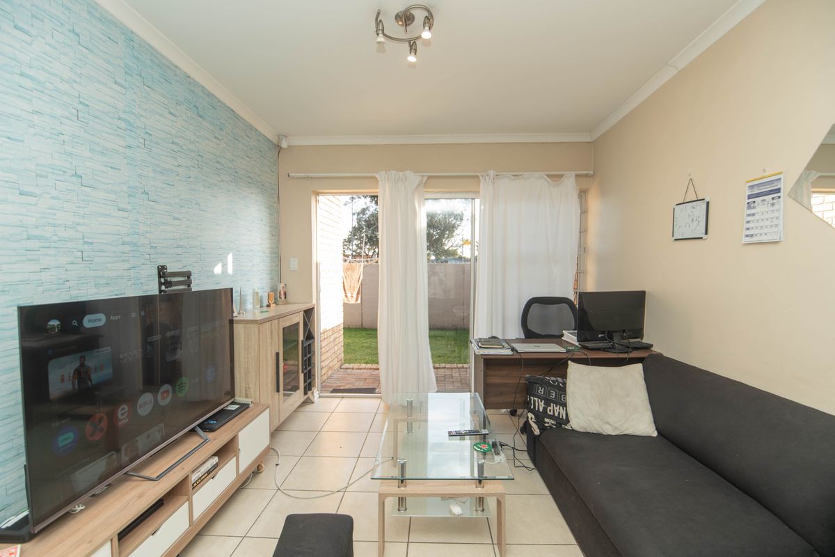 A living room featuring tiled flooring, a textured accent wall, and a sliding glass door providing direct access to the rear garden area.