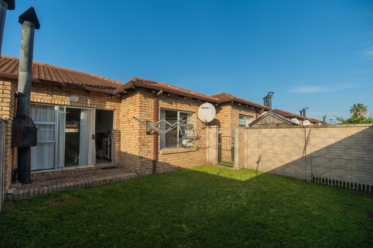 Rear view of the townhouse featuring a private garden, brick facade, sliding door access, and an external fireplace chimney.