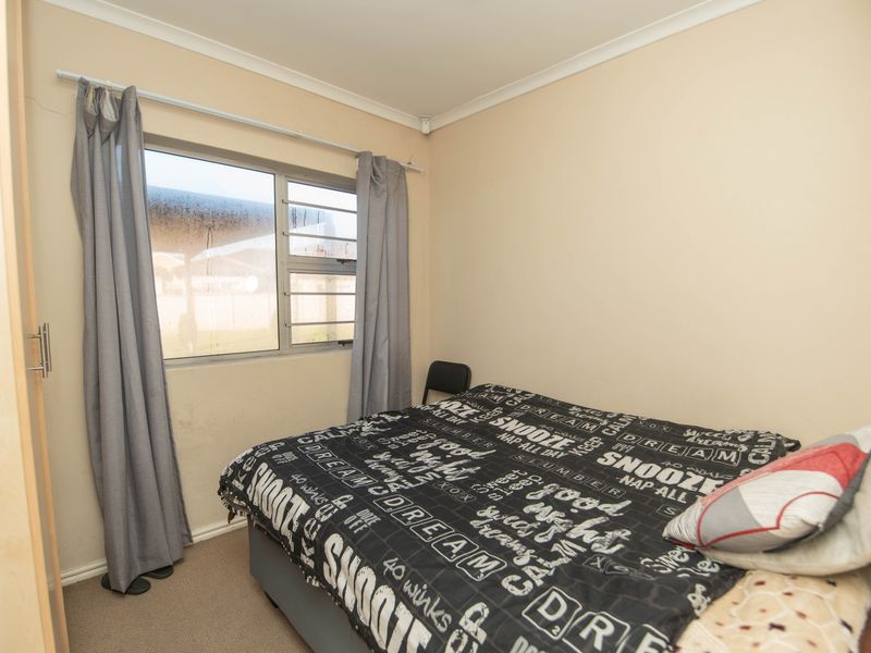 A standard bedroom featuring a built-in wardrobe, neutral wall finishes, and an aluminium-framed window with views to the exterior.