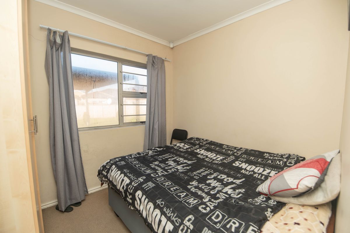 A standard bedroom featuring a built-in wardrobe, neutral wall finishes, and an aluminium-framed window with views to the exterior.