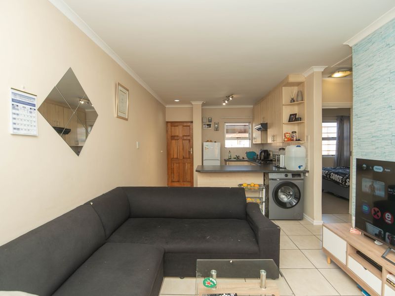 Open-plan living area featuring a compact kitchen with built-in cabinetry, tiled flooring, and direct access to adjacent rooms.