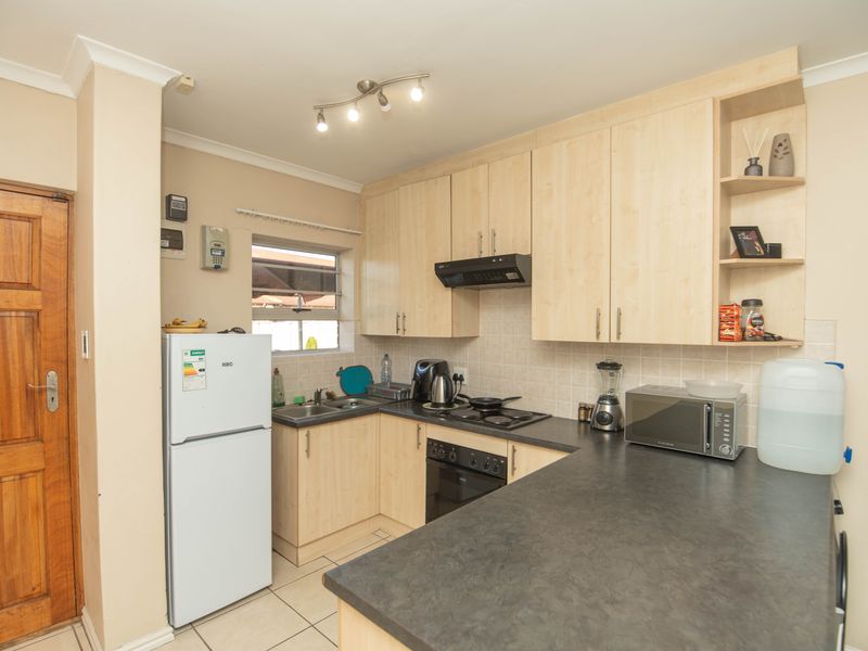 A functional kitchen featuring light wood-finish cabinetry, dark countertops, built-in oven and hob, and tiled flooring.