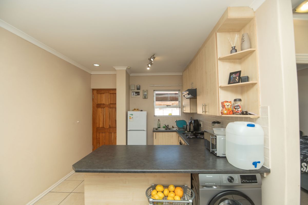 A functional kitchen featuring light wood-finish cabinetry, dark laminate countertops, a built-in hob with extractor, and tiled flooring with an integrated laundry appliance space.