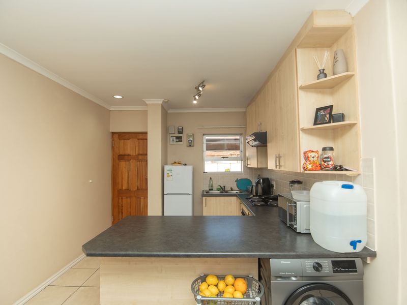A functional kitchen featuring light wood-finish cabinetry, dark laminate countertops, a built-in hob with extractor, and tiled flooring with an integrated laundry appliance space.