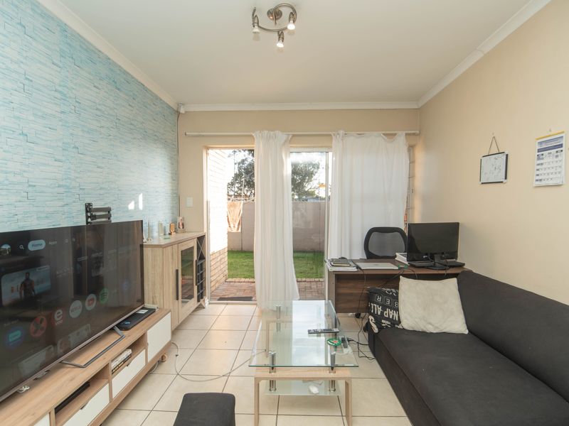 A living room featuring tiled flooring, a textured accent wall, and a sliding glass door providing direct access to the rear garden area.