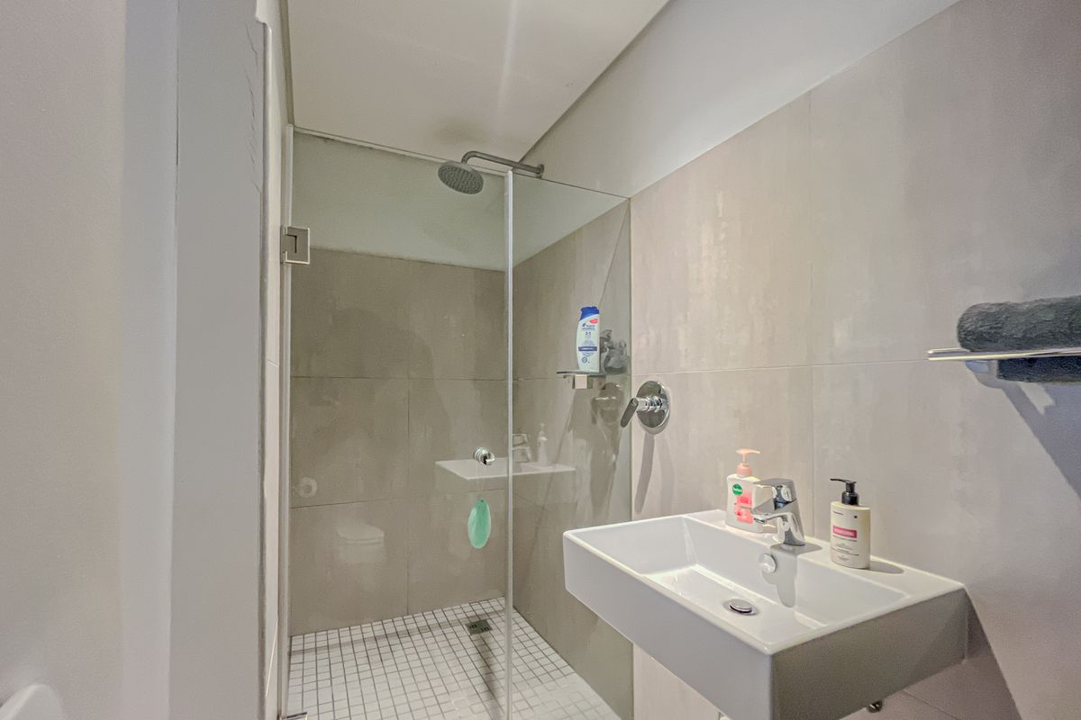 Modern bathroom featuring a wall-mounted basin with mixer tap and a glass-enclosed shower with tiled finishes.