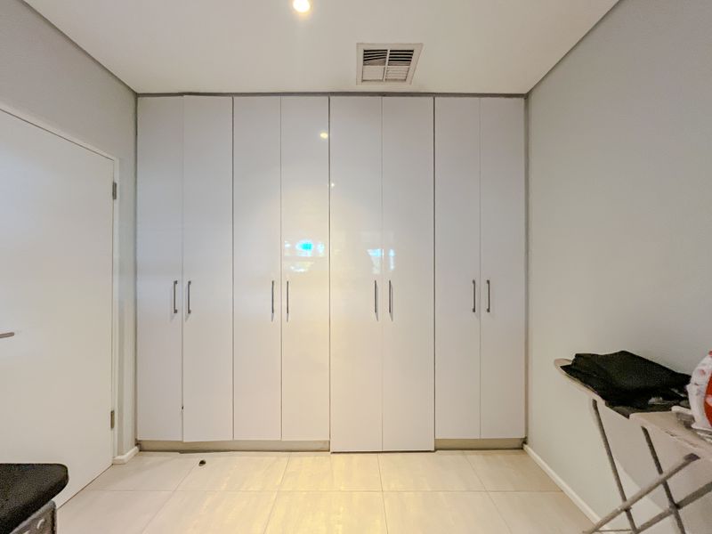 A clean, minimalist bedroom featuring floor-to-ceiling white built-in cupboards, neutral tiled flooring, and recessed ceiling lighting.