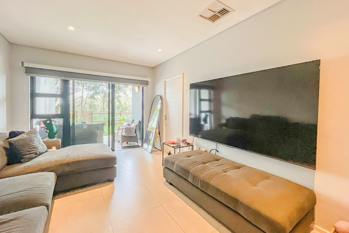 A bright living room featuring large sliding glass doors leading to a patio, tiled flooring, and recessed lighting.