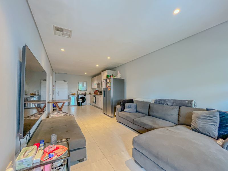 An open-plan living and kitchen area featuring tiled flooring, recessed lighting, and a functional kitchen layout with built-in cabinetry and appliances.