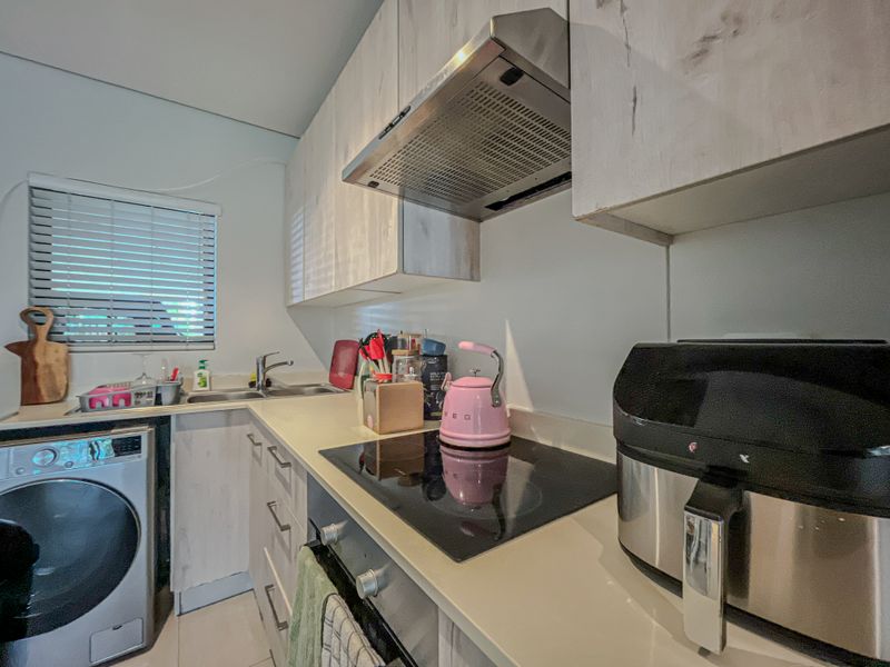 Compact kitchen featuring modern laminate cabinetry, built-in oven, electric hob with extractor fan, and an integrated washing machine under the counter.