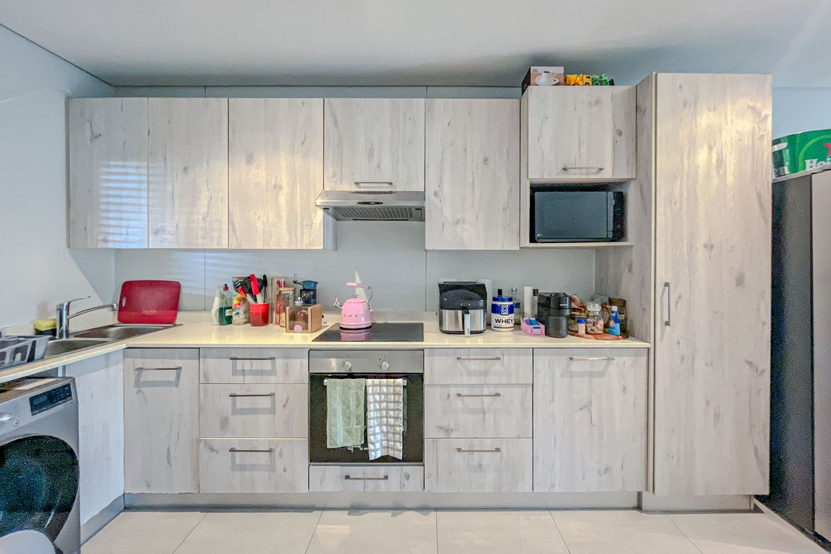 A functional kitchen featuring light wood-grain cabinetry, integrated appliances including an oven and hob, and tiled flooring.