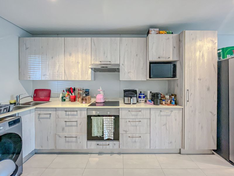 A functional kitchen featuring light wood-grain cabinetry, integrated appliances including an oven and hob, and tiled flooring.