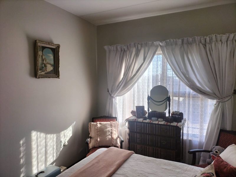 A cozy bedroom featuring neutral wall tones, natural light through window treatments, and functional electrical points.