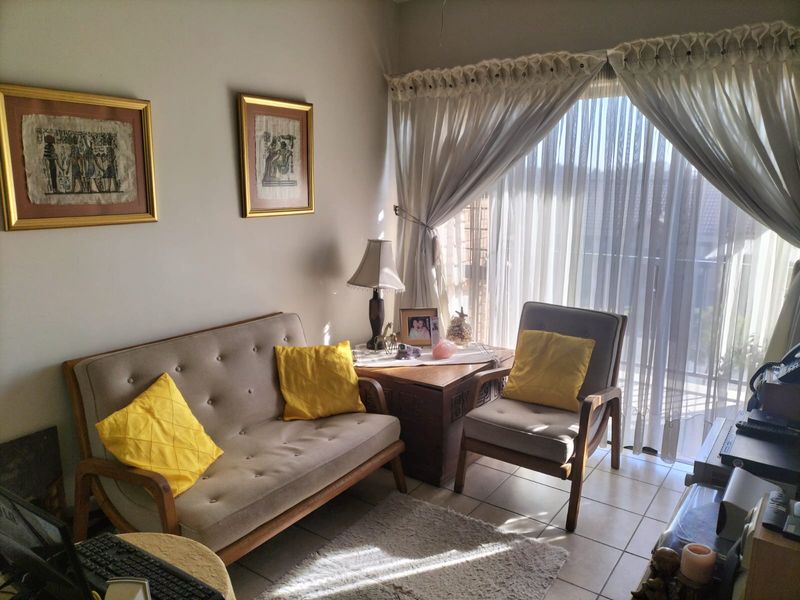 A cozy living room area featuring tiled flooring and a large sliding glass door with curtains, providing natural light and access to the balcony.