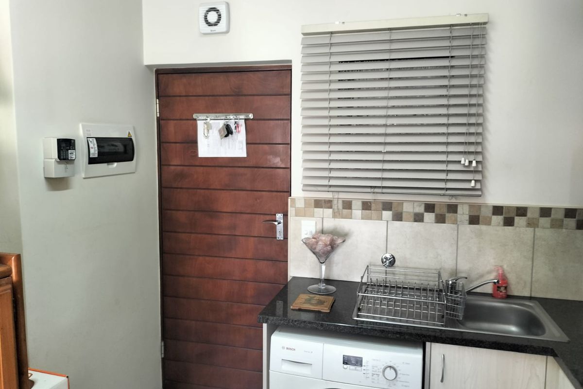 A functional laundry area featuring built-in cabinetry, a stainless steel sink, tiled backsplash, and an integrated extractor fan.