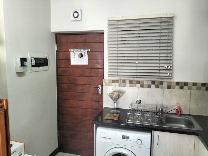 A functional laundry area featuring built-in cabinetry, a stainless steel sink, tiled backsplash, and an integrated extractor fan.