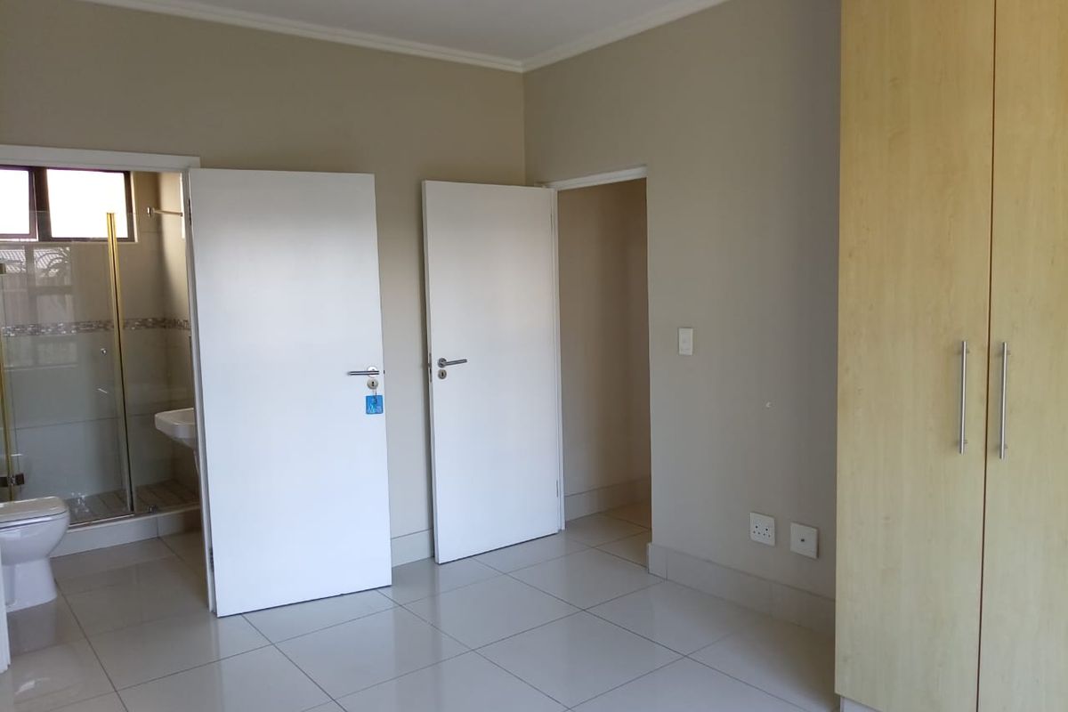 A clean, empty bedroom featuring light-toned tiled flooring, built-in wooden cupboards, and direct access to an en-suite bathroom.