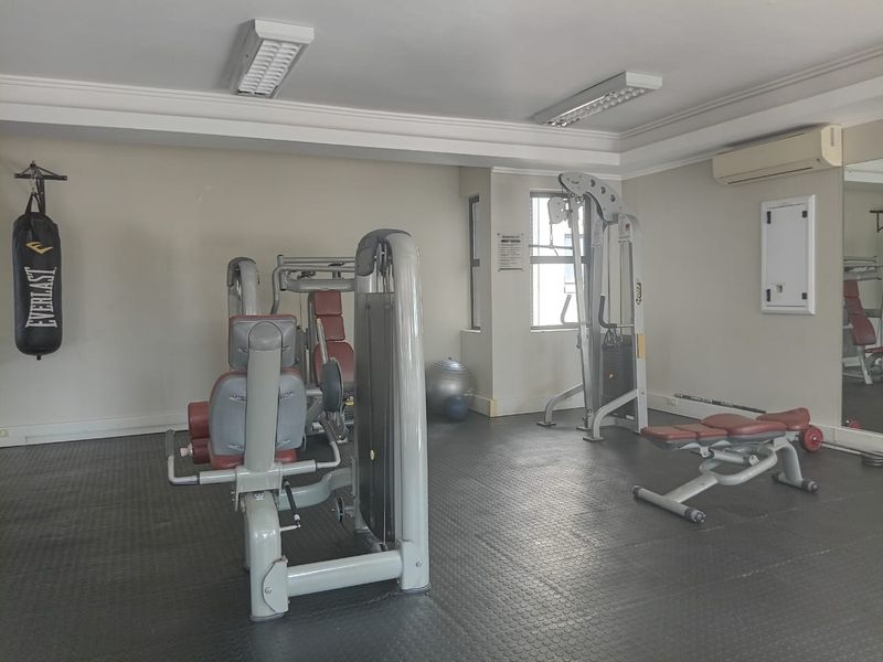 A functional apartment gym facility featuring rubber flooring, mirrored walls, and an integrated air conditioning unit.