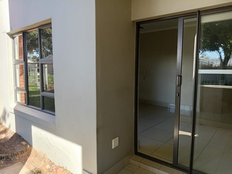 Exterior view of an apartment patio area featuring a sliding glass door and aluminium window frames with tiled flooring.