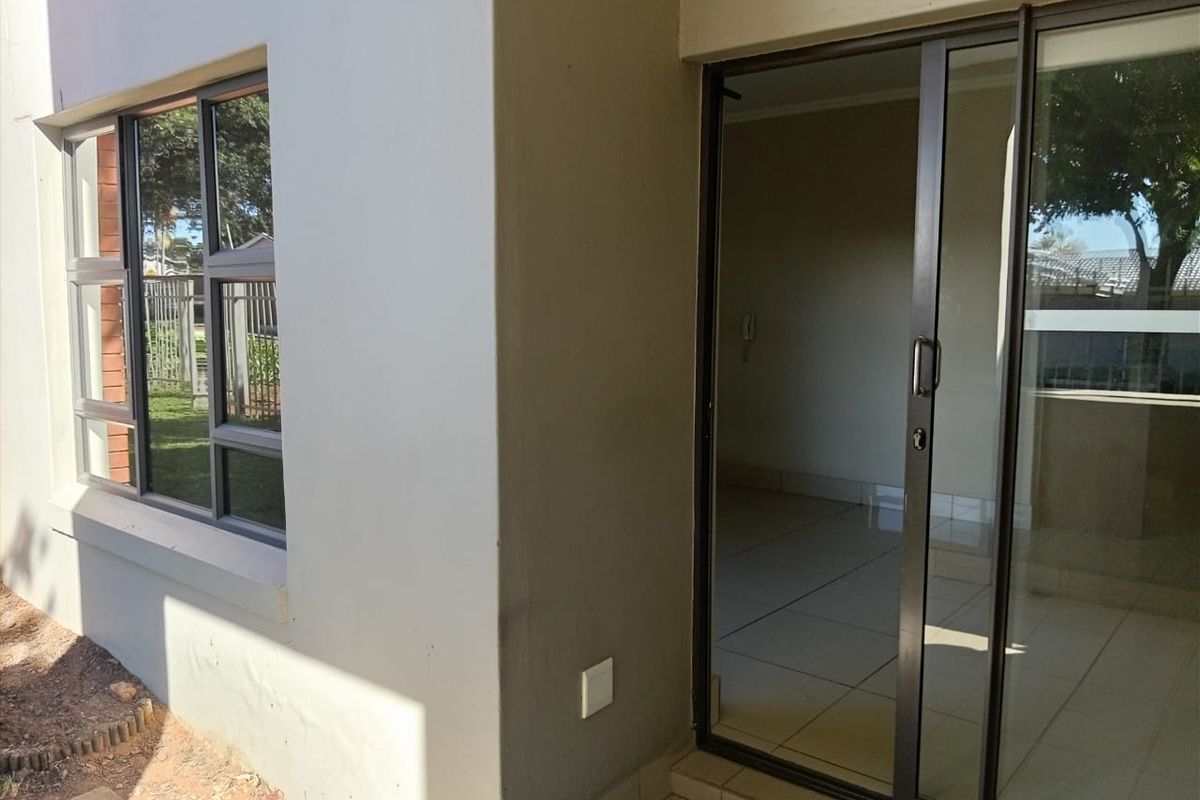 Exterior view of an apartment patio area featuring a sliding glass door and aluminium window frames with tiled flooring.
