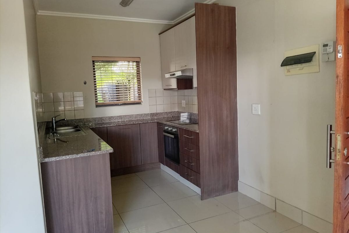 A clean and functional kitchen featuring modern wood-finish cabinetry, granite countertops, built-in oven and hob, and neutral tiled flooring.