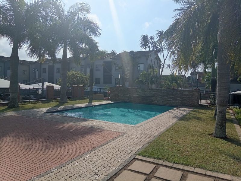 A well-maintained communal swimming pool area featuring brick paving, a stone-clad feature wall, and landscaped surroundings within an apartment complex.